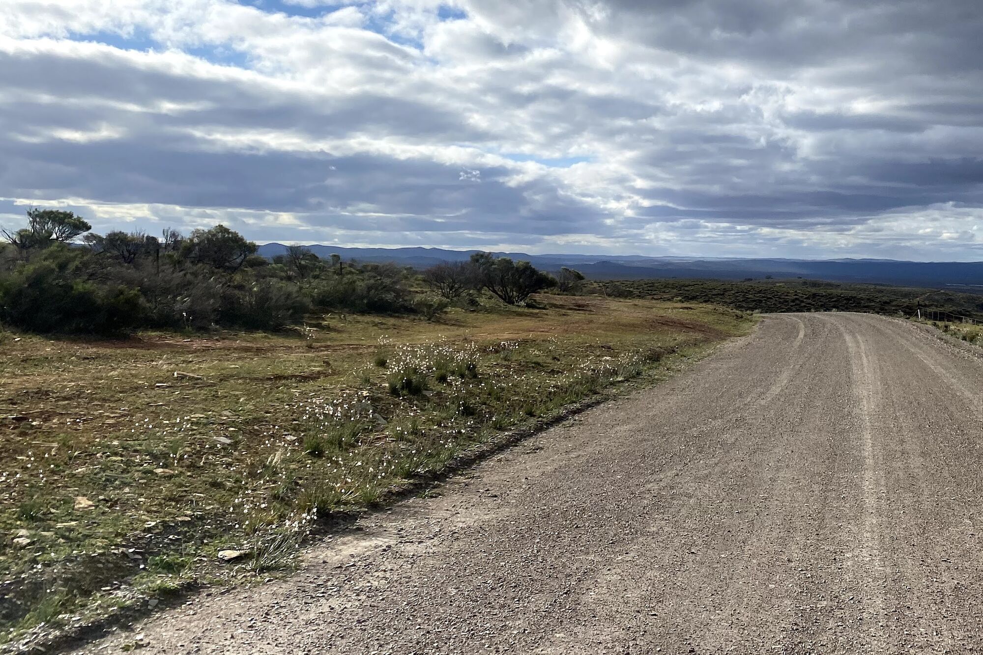 A gravel road curving toward distant ranges under heavy cloud